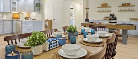 A modern kitchen with white cabinets, a dining table set with blue glass candle holders, white plates, and a potted plant.