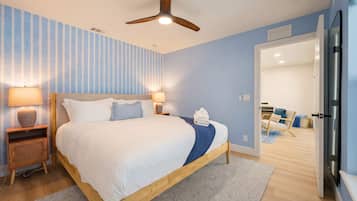 Habitación de hotel con cama, lámparas de noche, ventilador de techo y vista a la habitación contigua.
