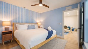 Quarto de hotel com cama, abajures, ventoinha no teto e vista para o quarto vizinho.