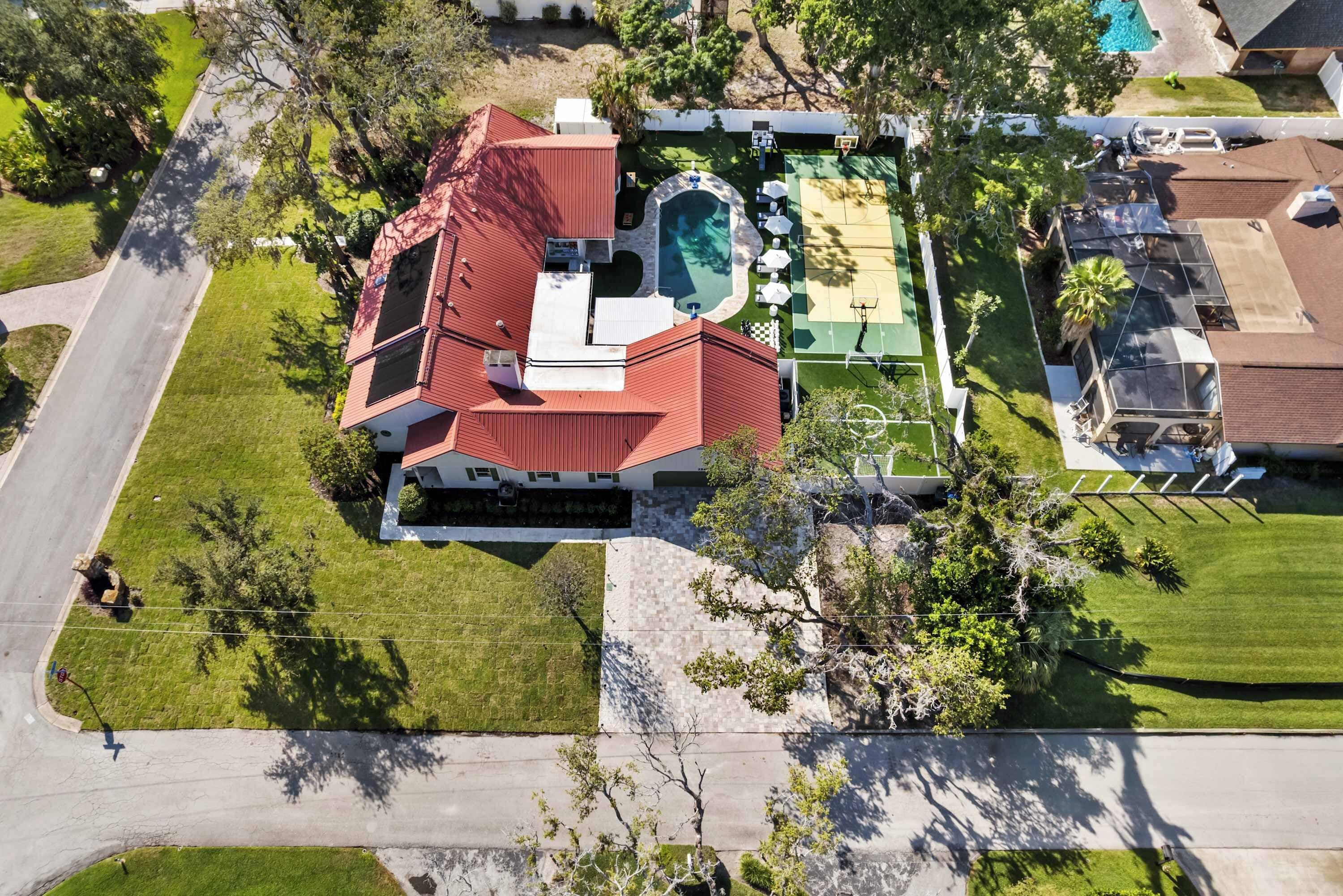An aerial view of a house with a swimming pool, tennis court, and a well-maintained lawn.