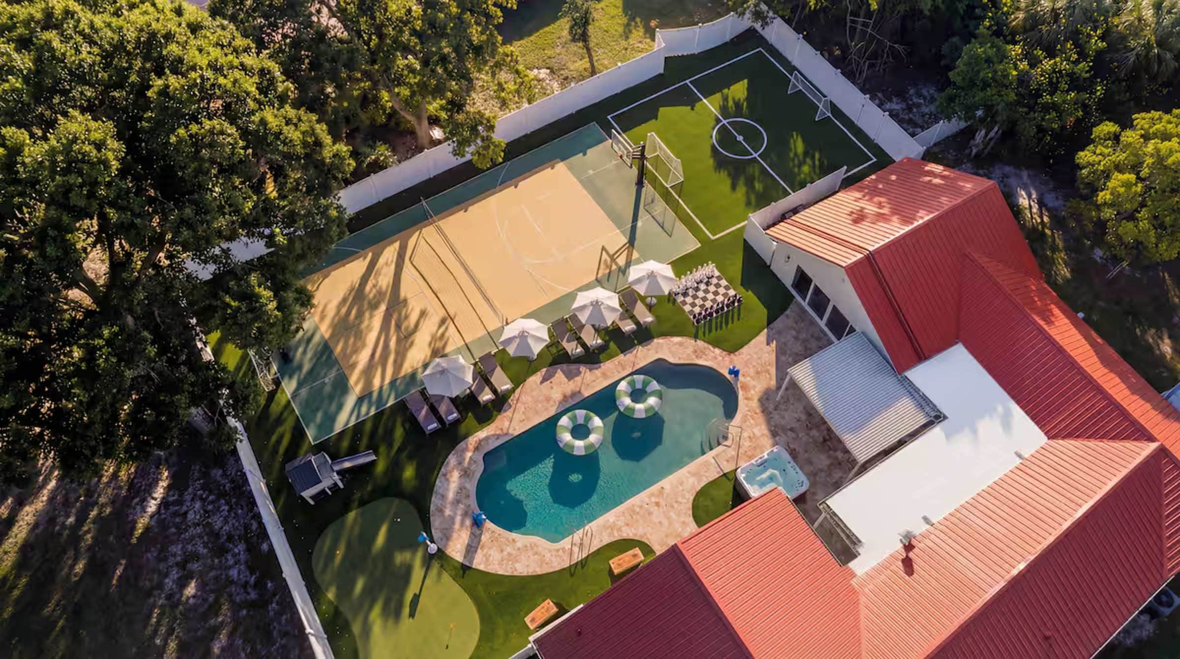 An aerial view of a property with a tennis court, a swimming pool, and a covered patio area.