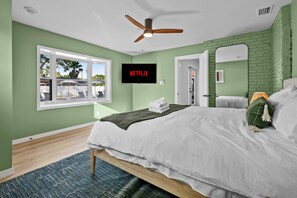 A bedroom with a bed, a ceiling fan, a TV mounted on the wall, and a window with a view of outdoor furniture. - Heated Pool—Gym—Hot tub—Pickleball—Near Beach (Largo)