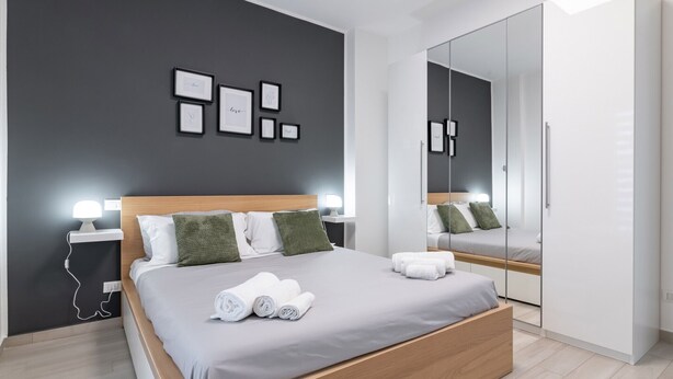 Een moderne slaapkamer met een bed, nachtkastjes, een spiegel en een kledingkast.