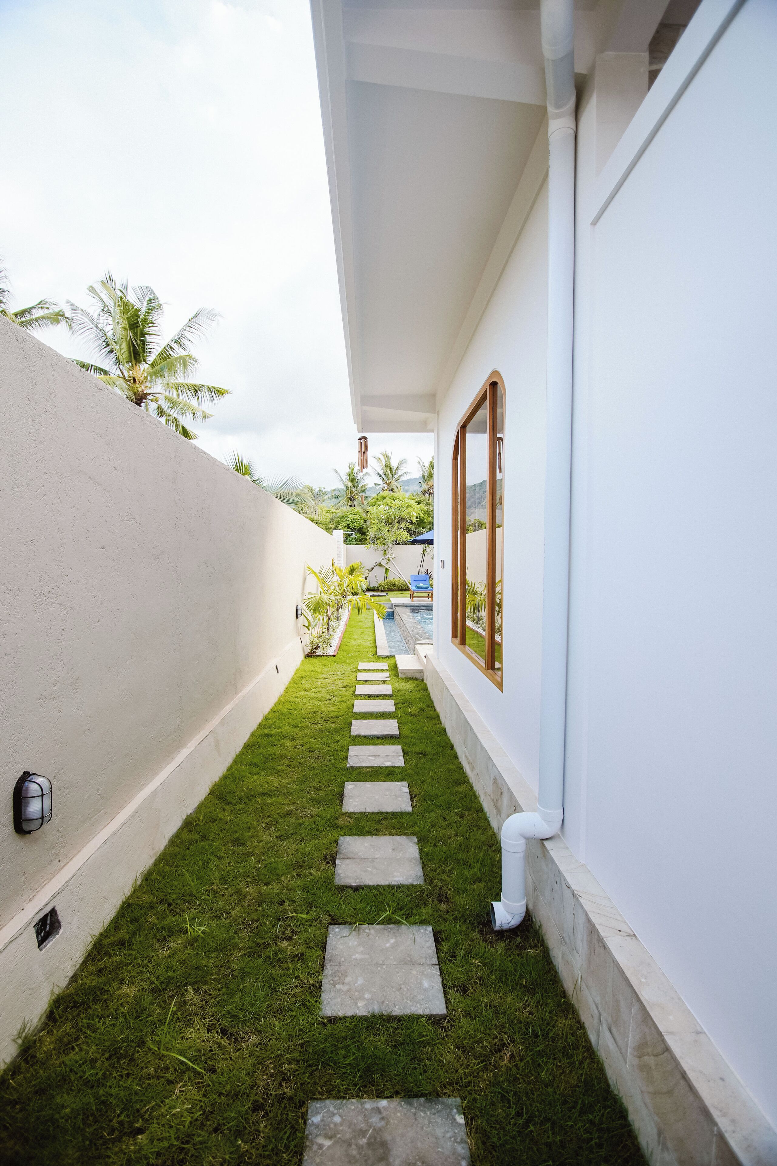 A narrow pathway with a white wall on one side and a pool on the other.