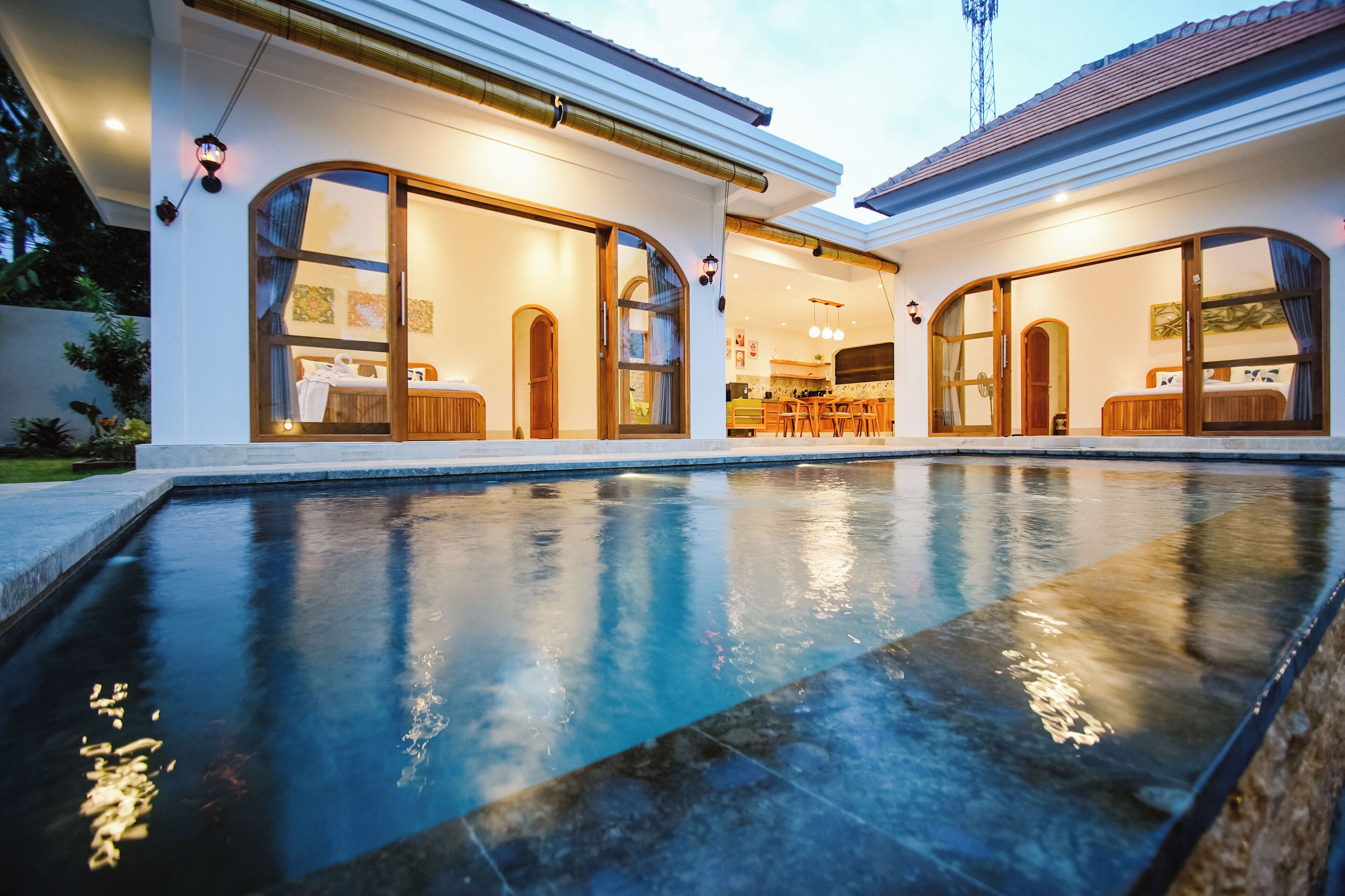 Une maison moderne dotée d’une piscine, de grandes portes vitrées donnant sur un espace repas et d’une cuisine visible à travers le verre.