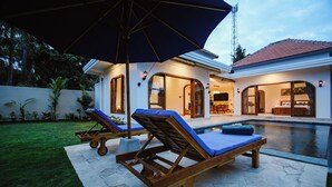 Un área junto a la piscina con dos sillones de descanso y una sombrilla grande.