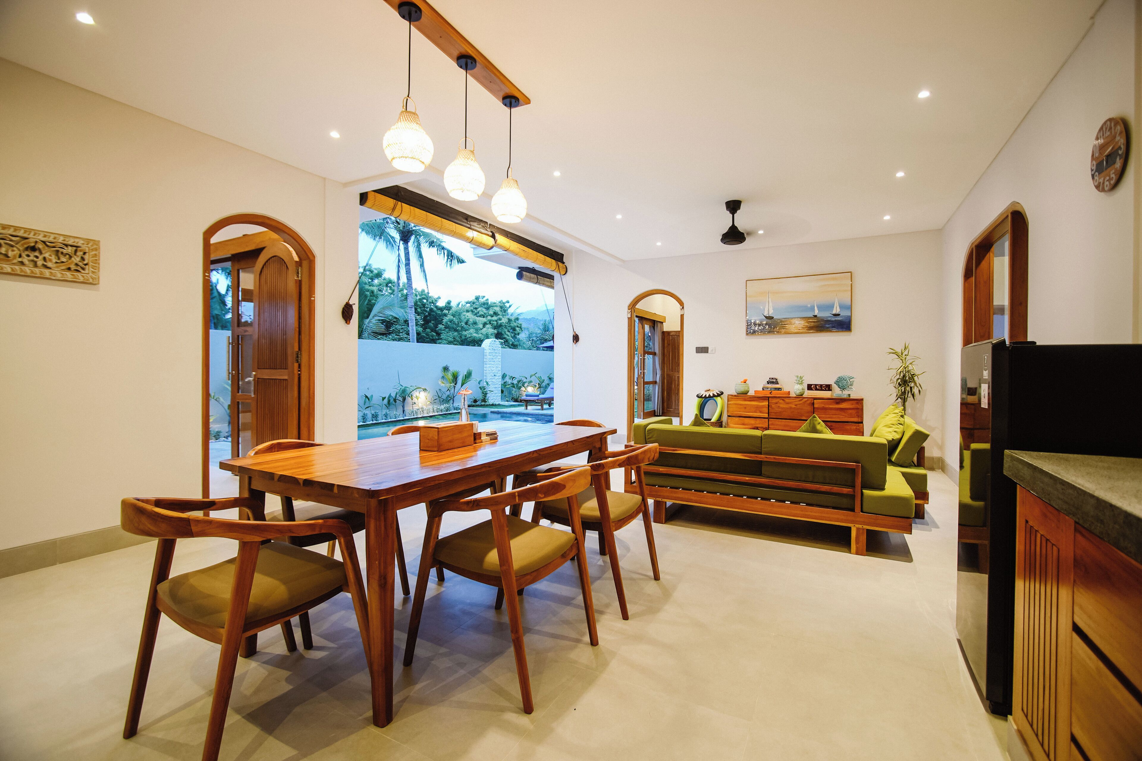 A dining area with a wooden table and chairs, a sofa, and a kitchen area with a refrigerator.