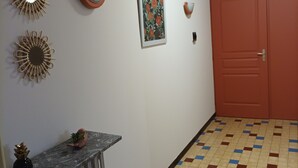 Een gang met een betegelde vloer, een deur en wanddecoratie, waaronder een spiegel en een lijstwerk met een afbeelding.