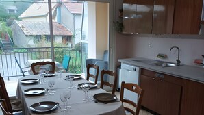 Een eetgedeelte met een ronde tafel voor vier personen, houten stoelen, een keuken met houten kasten en uitzicht op huizen door een groot raam.