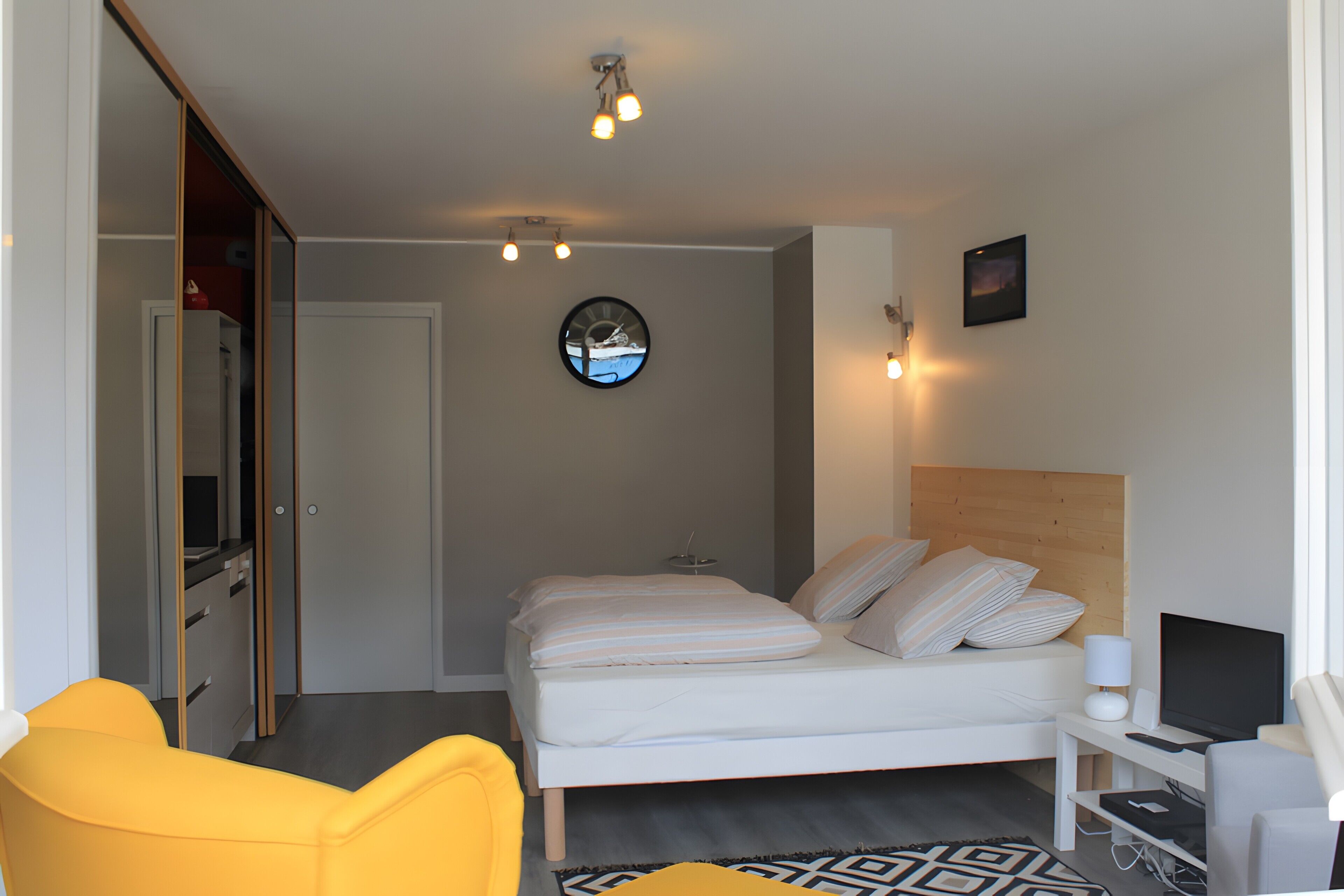 Habitación de hotel con cama, escritorio con computadora, silla, reloj y un cuadro en la pared.