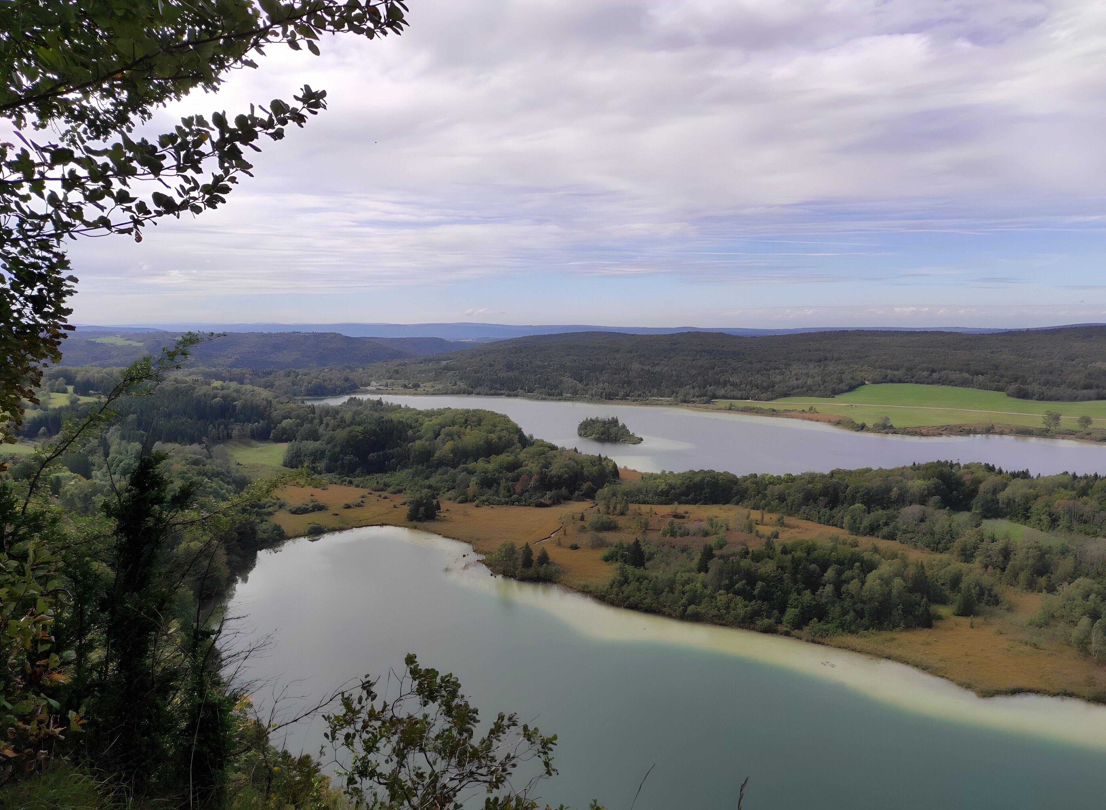 A panoramic view of a lake surrounded by forested hills and a clear sky.