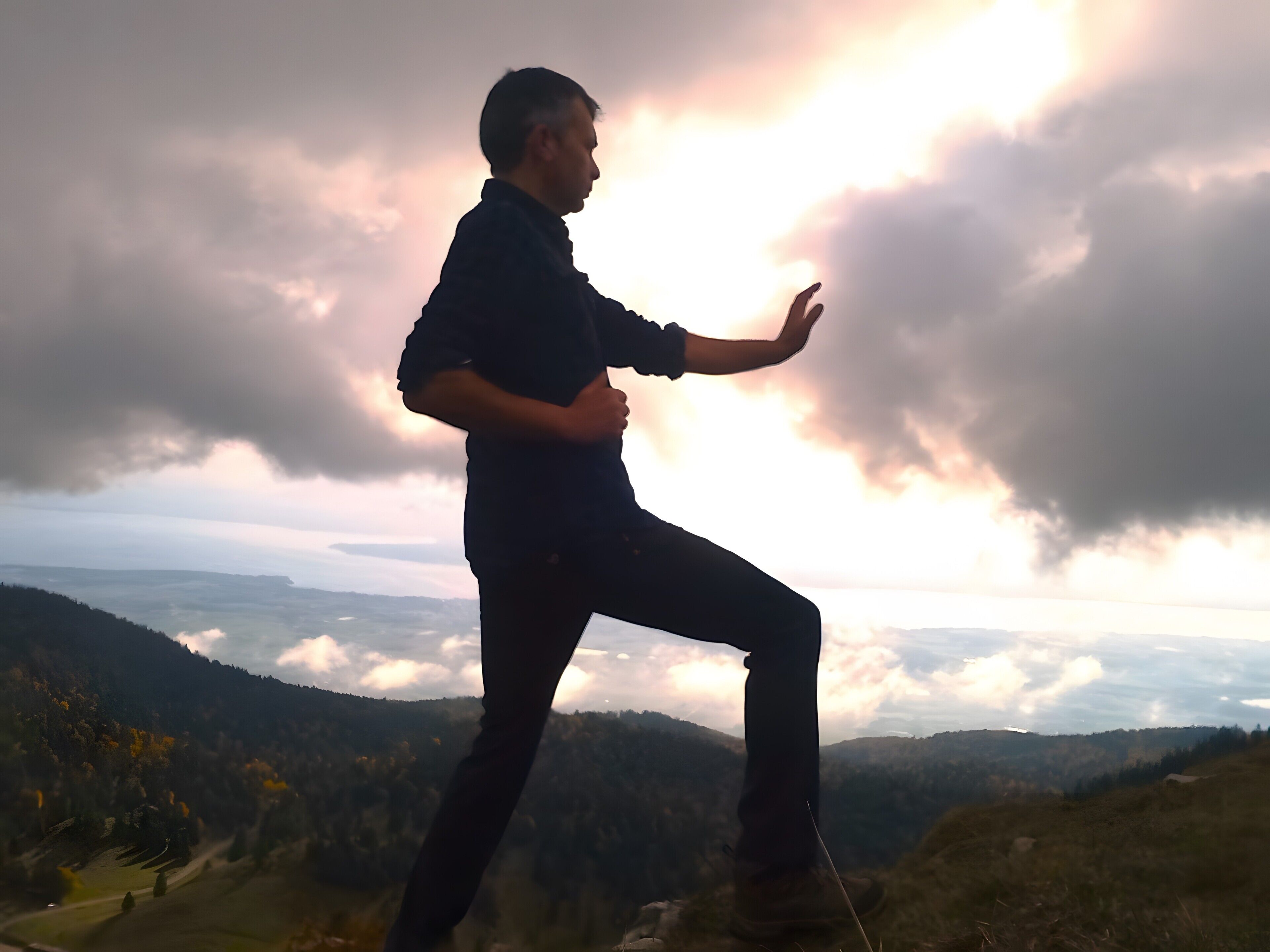 Eine Person steht auf einem Hügel mit weiter Aussicht über ein Tal und Berge.