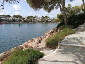 A coastal walkway with a concrete path leading to a rocky shoreline. - Villa Ramina located on the seafront in the old town of Cala Dor. (Santanyí)
