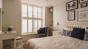 A bedroom with a bed, a desk, a chair, a nightstand, and a window with blinds. - Old Village Shop, Ambleside, central, cosy retreat (Ambleside)