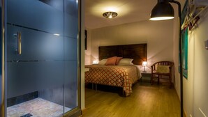 Quarto com cama, cabeceira de madeira, mesa de cabeceira, cadeira, luminária e porta com painéis de vidro jateado.