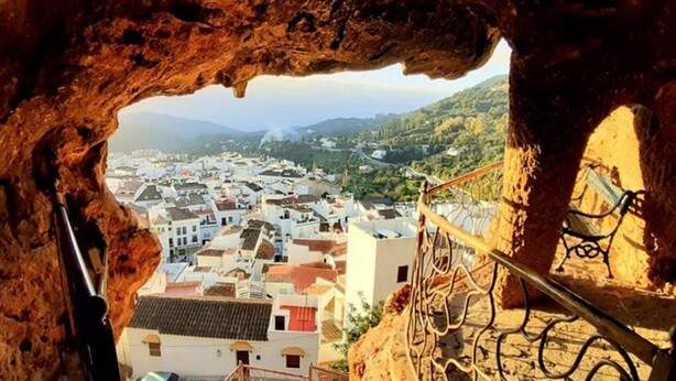 Vista de uma abertura de caverna sobre uma cidade com edifícios brancos e telhados vermelhos.