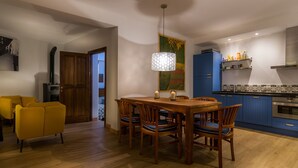 Uma área de refeições com mesa e cadeiras de madeira, luminária pendente e cozinha com armários azuis e fogão.