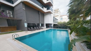 An outdoor swimming pool with lounge chairs and a modern building in the background.