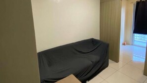 Une petite pièce, peu meublée, avec un lit simple, une petite table et une fenêtre avec des rideaux.