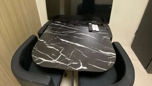 Une petite pièce moderne, avec une table en marbre noir, deux chaises noires et un grand miroir au mur.