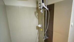 Une petite salle de douche carrelée, équipée d’un pommeau de douche à main, d’un robinet mural et d’un panneau de commande.