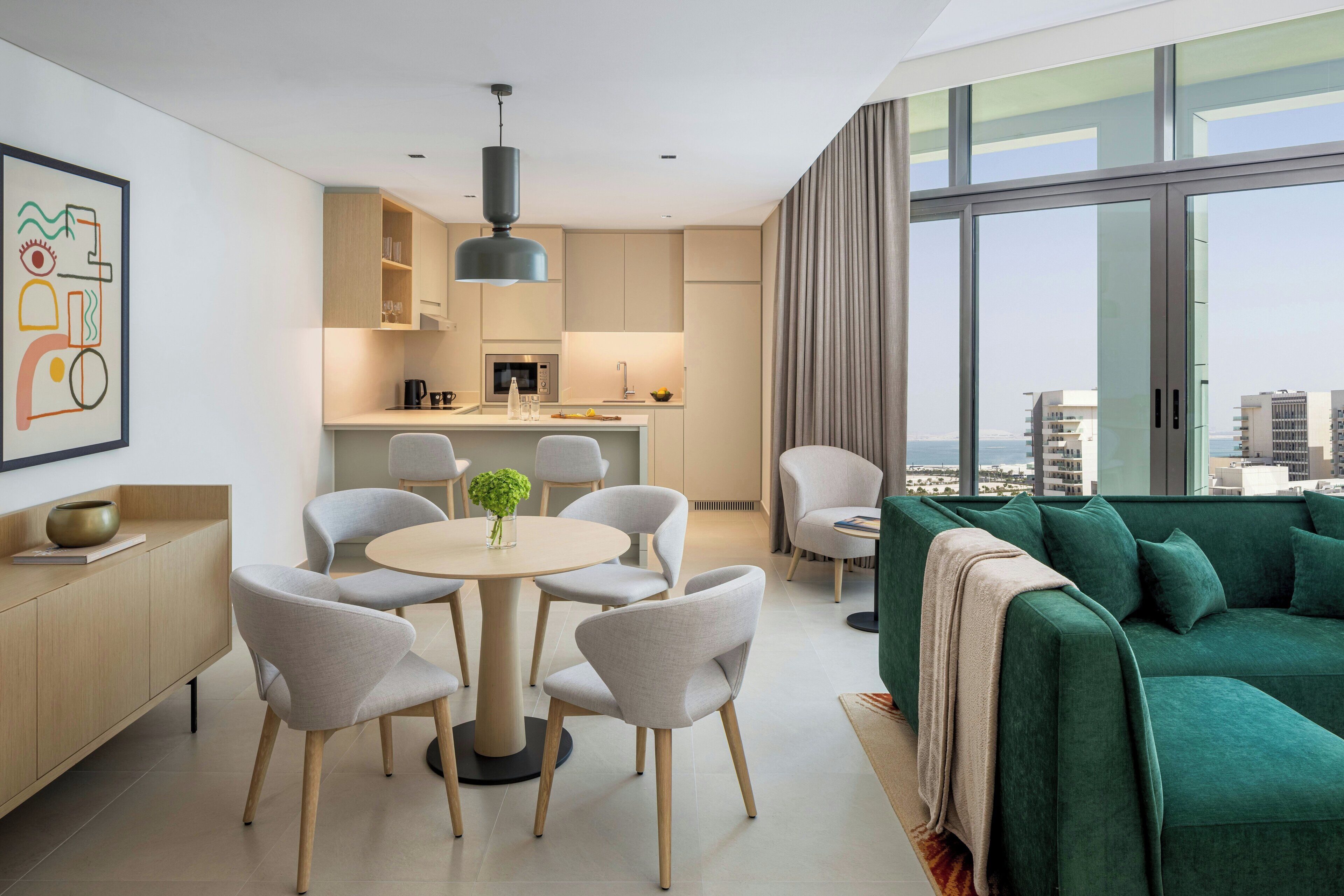A modern living space with a dining area, kitchen, and a green sofa with a view.