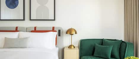 A hotel room with a bed, a green armchair, a nightstand with a lamp, and two abstract paintings on the wall.