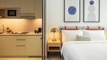 Una habitación de hotel moderna con kitchenette, una cama con ropa blanca y dos obras de arte abstracto en la pared.