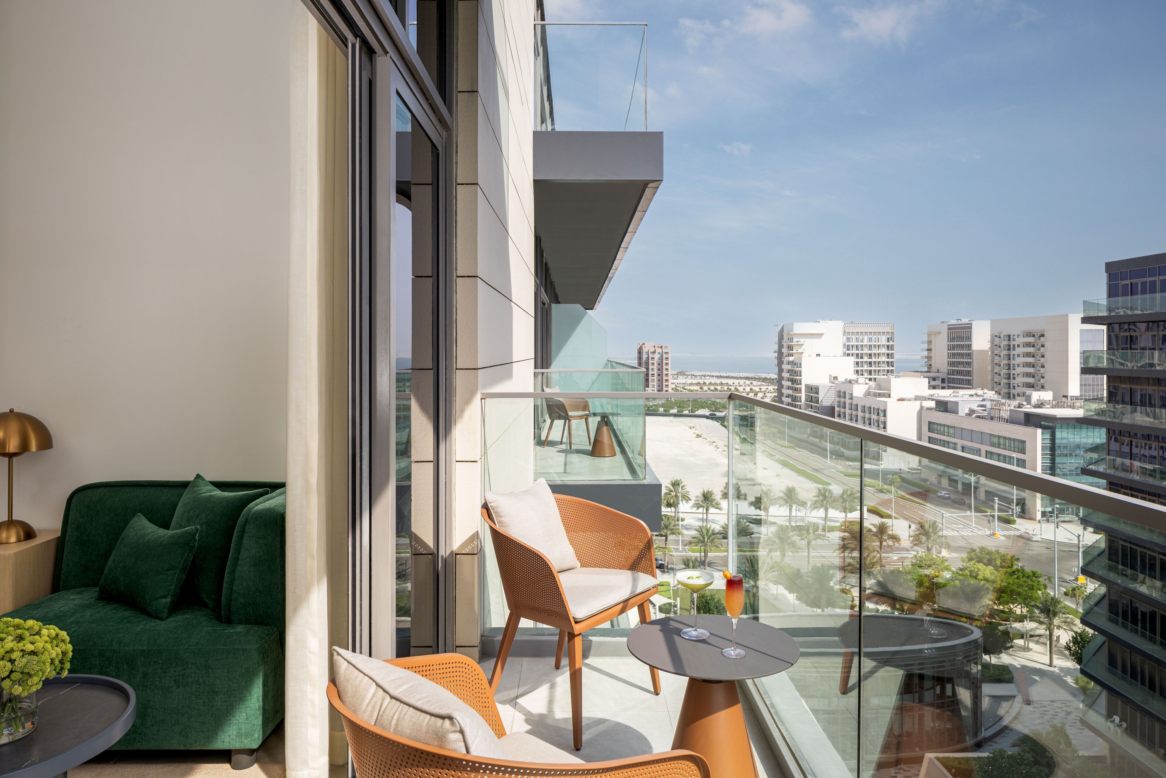 A balcony with a sofa, chairs, and a table, overlooking a cityscape and beach.