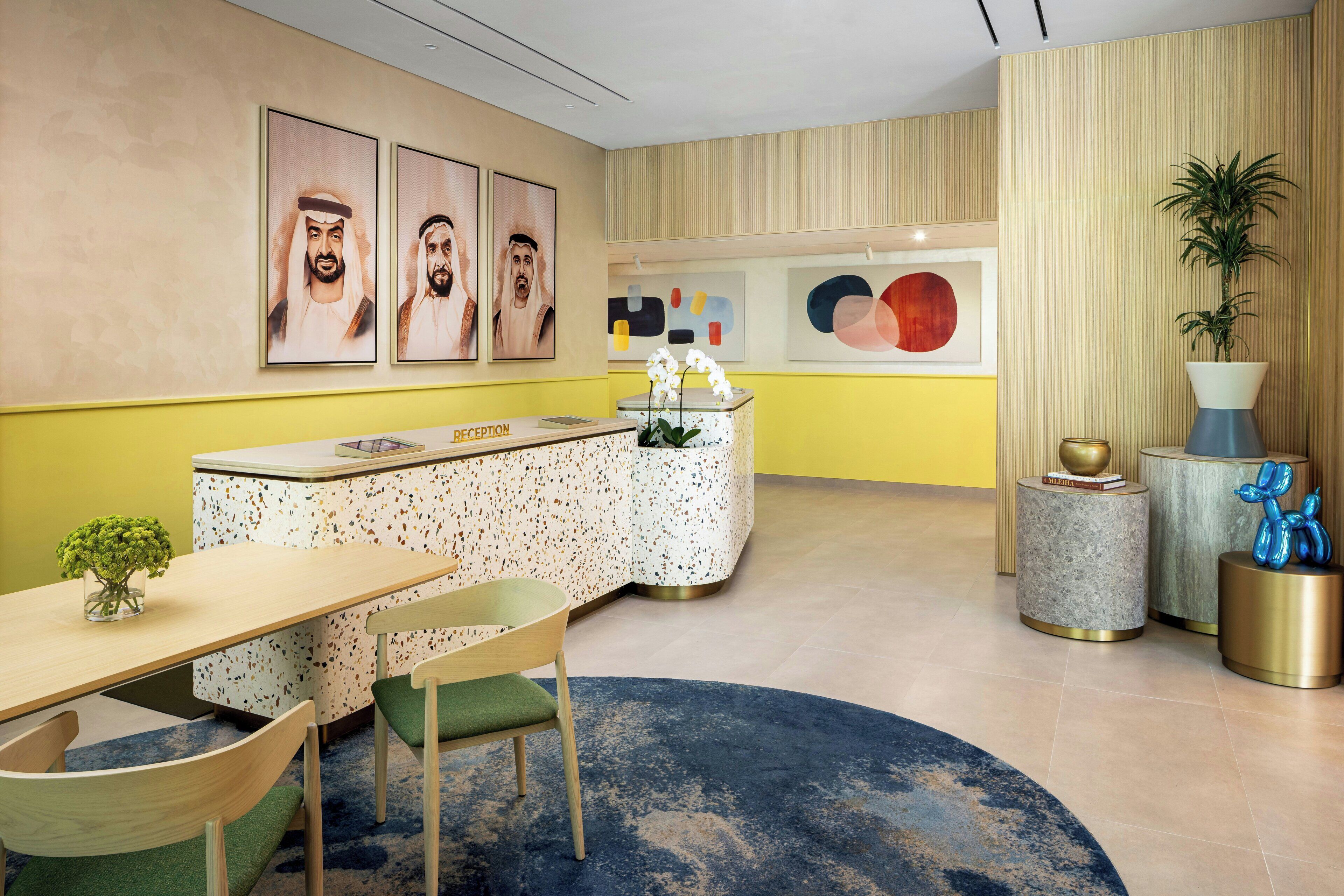 A reception area with a reception desk, chairs, a round table, a blue rug, and artwork on the walls.