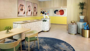 A reception area with a reception desk, chairs, a round table, a blue rug, and artwork on the walls.