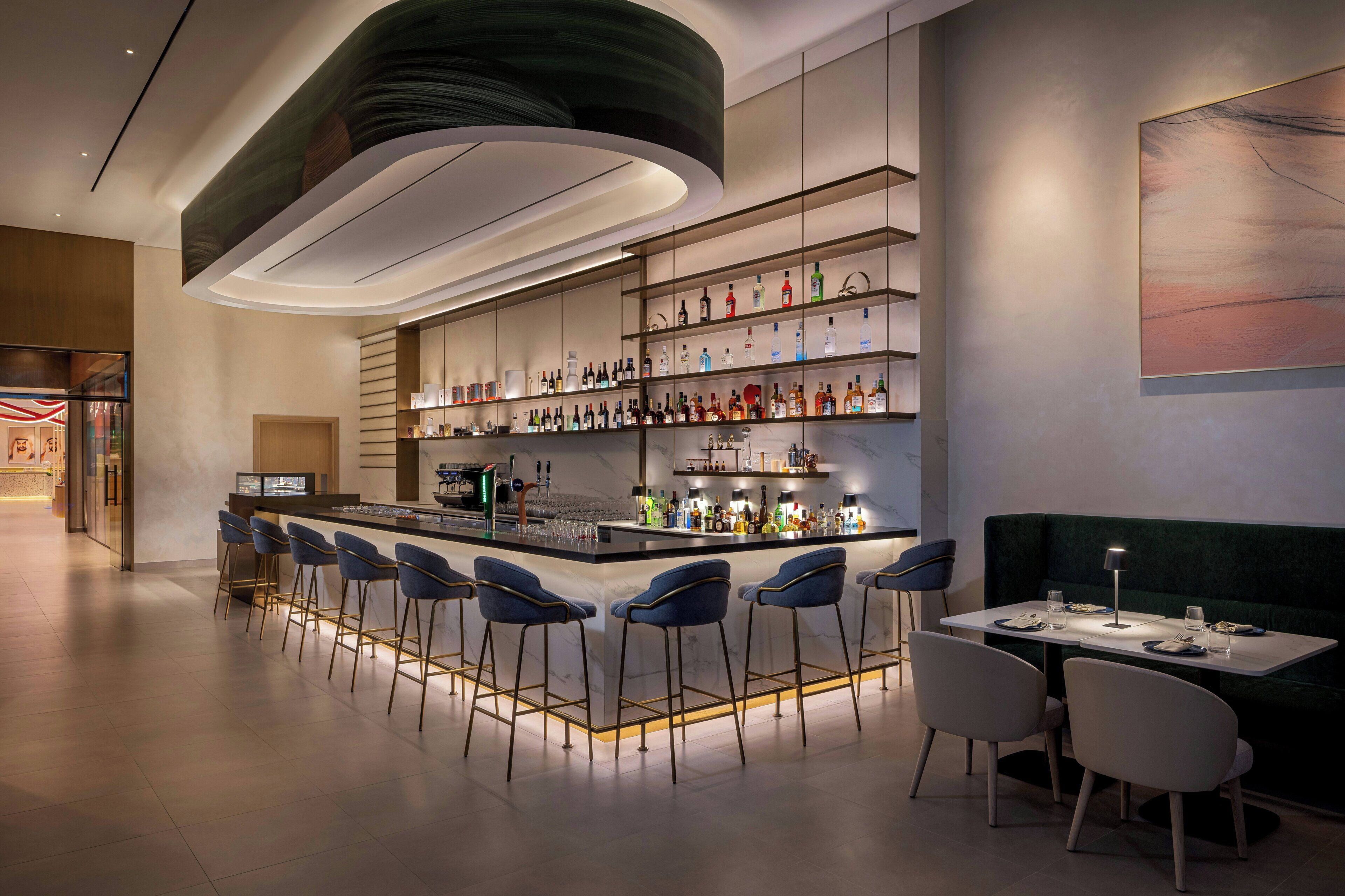 A modern bar area with a long counter, multiple bar stools, and a seating area with a table and chairs.