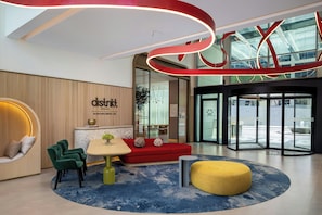 A modern interior with a red sofa, green chairs, a yellow ottoman, and a sign reading 'district social'. - Bloom Arjaan By Rotana (Abu Dhabi)