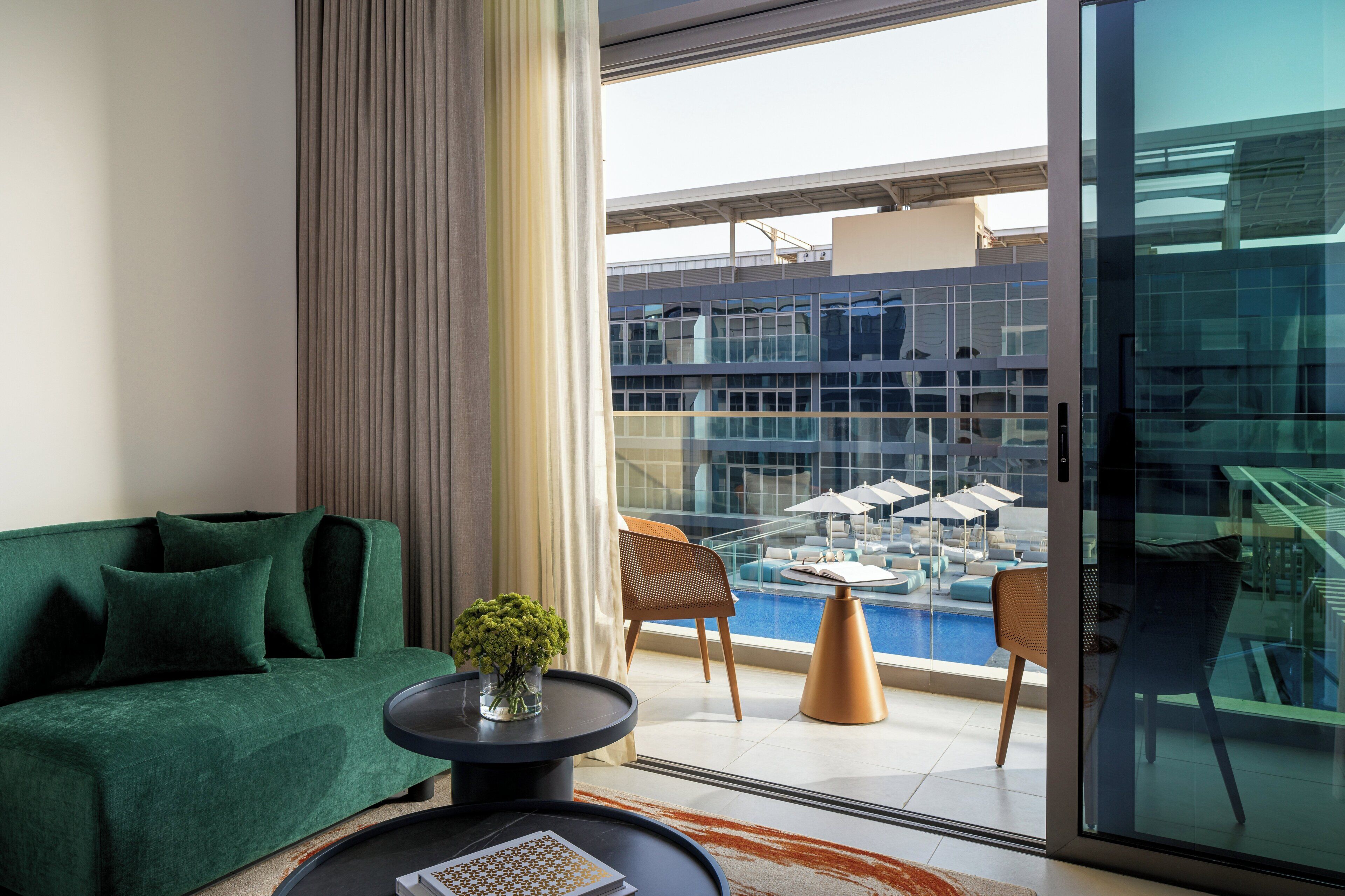 A modern living room with a green sofa, a coffee table, and a view of a rooftop pool area.