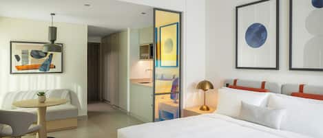 Habitación de hotel moderna con una cama grande, un escritorio, una silla y una mesita. Se observan obras de arte enmarcadas en las paredes y una ventana con vistas.