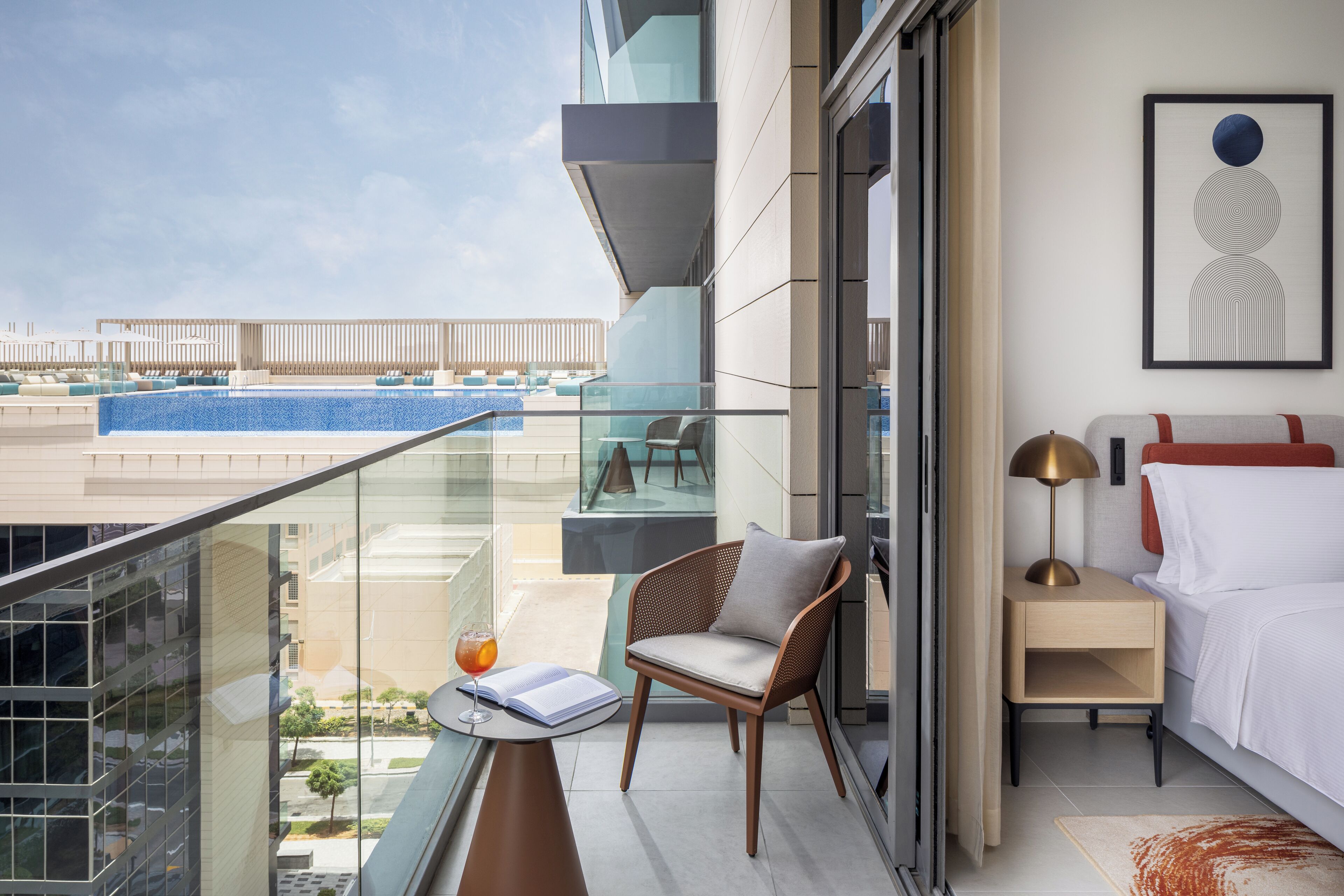 Un balcon donnant sur une piscine, une chaise, une table de chevet avec une lampe et un lit.