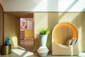 A modern interior with a curved seating area, a tall vase with a plant, and a sculptural piece on a pedestal. - Bloom Arjaan By Rotana (Abu Dhabi)