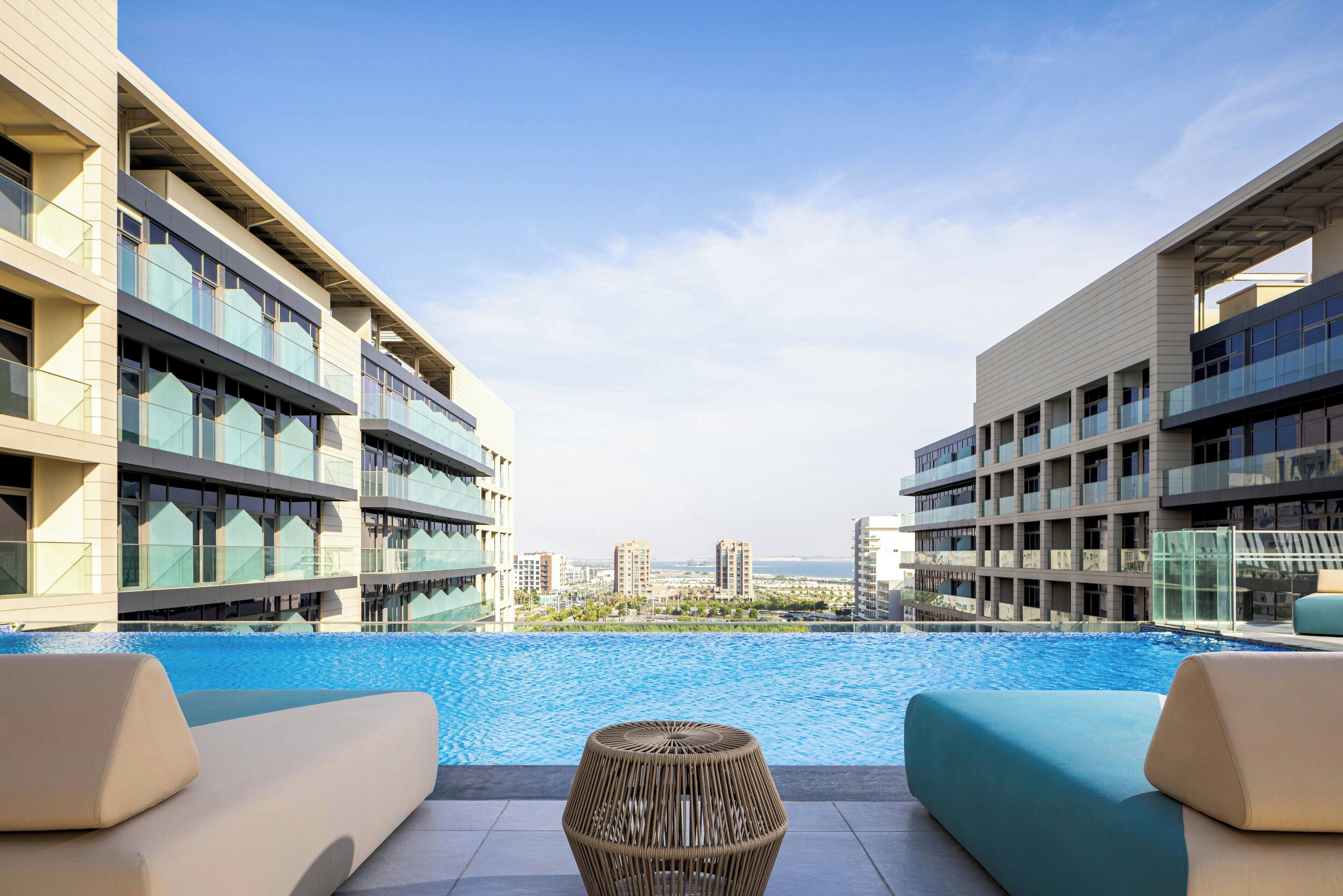 A modern hotel with a pool, outdoor seating, and a view of the cityscape.