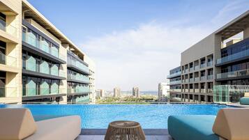 A modern hotel with a pool, outdoor seating, and a view of the cityscape.