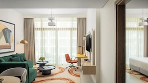 A modern living room with a green sofa, a coffee table, a TV mounted on the wall, and a large window with curtains. - Bloom Arjaan By Rotana (Abu Dhabi)