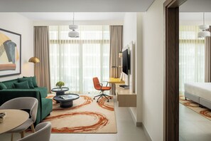 Een moderne woonkamer met een groene bank, een salontafel, een aan de muur bevestigde televisie en een groot raam met gordijnen.