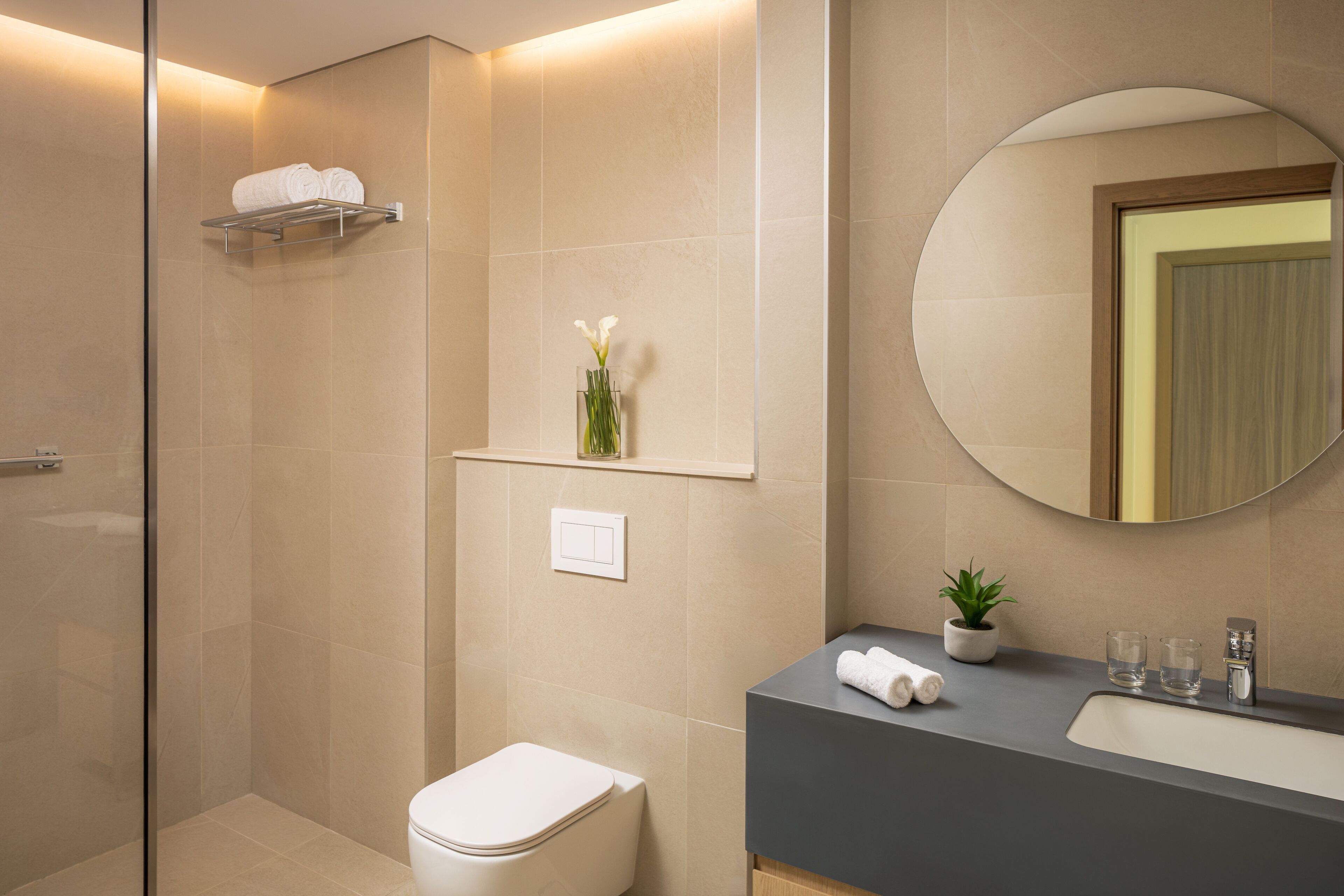 A modern bathroom with a toilet, sink, mirror, and a shower area.