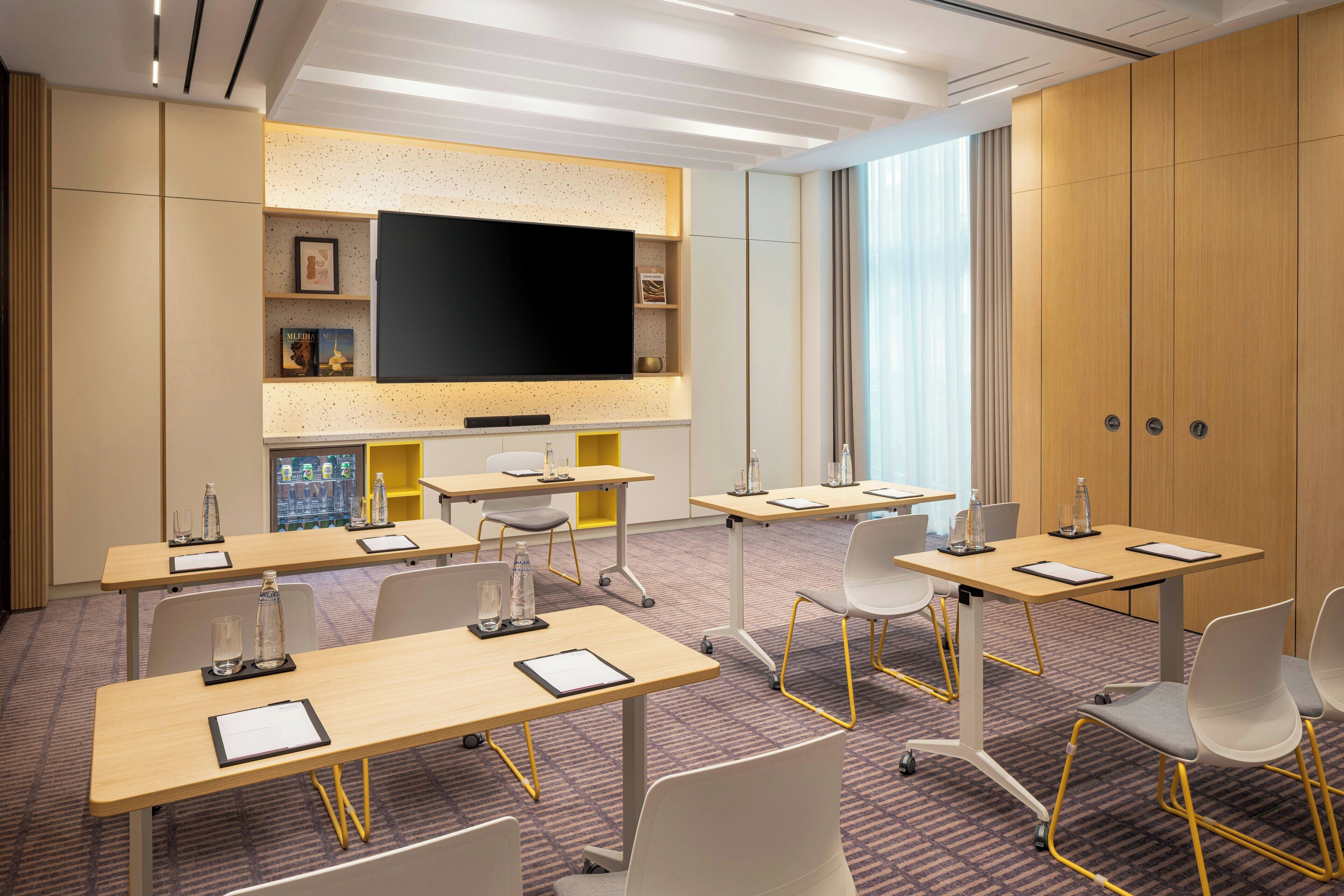 A conference room with a large flat-screen TV, multiple tables with chairs, and a carpeted floor.