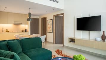 Una sala de estar moderna con un sofá verde, un televisor de pantalla plana y una cocina al fondo.
