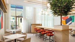 A modern hotel lobby with a bar area, seating, and a large indoor plant. - Bloom Arjaan By Rotana (Abu Dhabi)