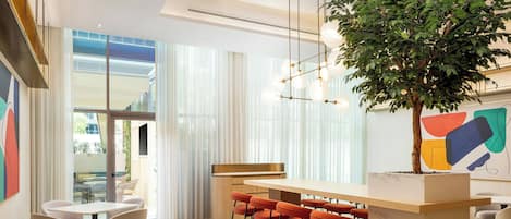 Un moderno vestíbulo de hotel con una zona de bar, asientos y una planta de interior grande.