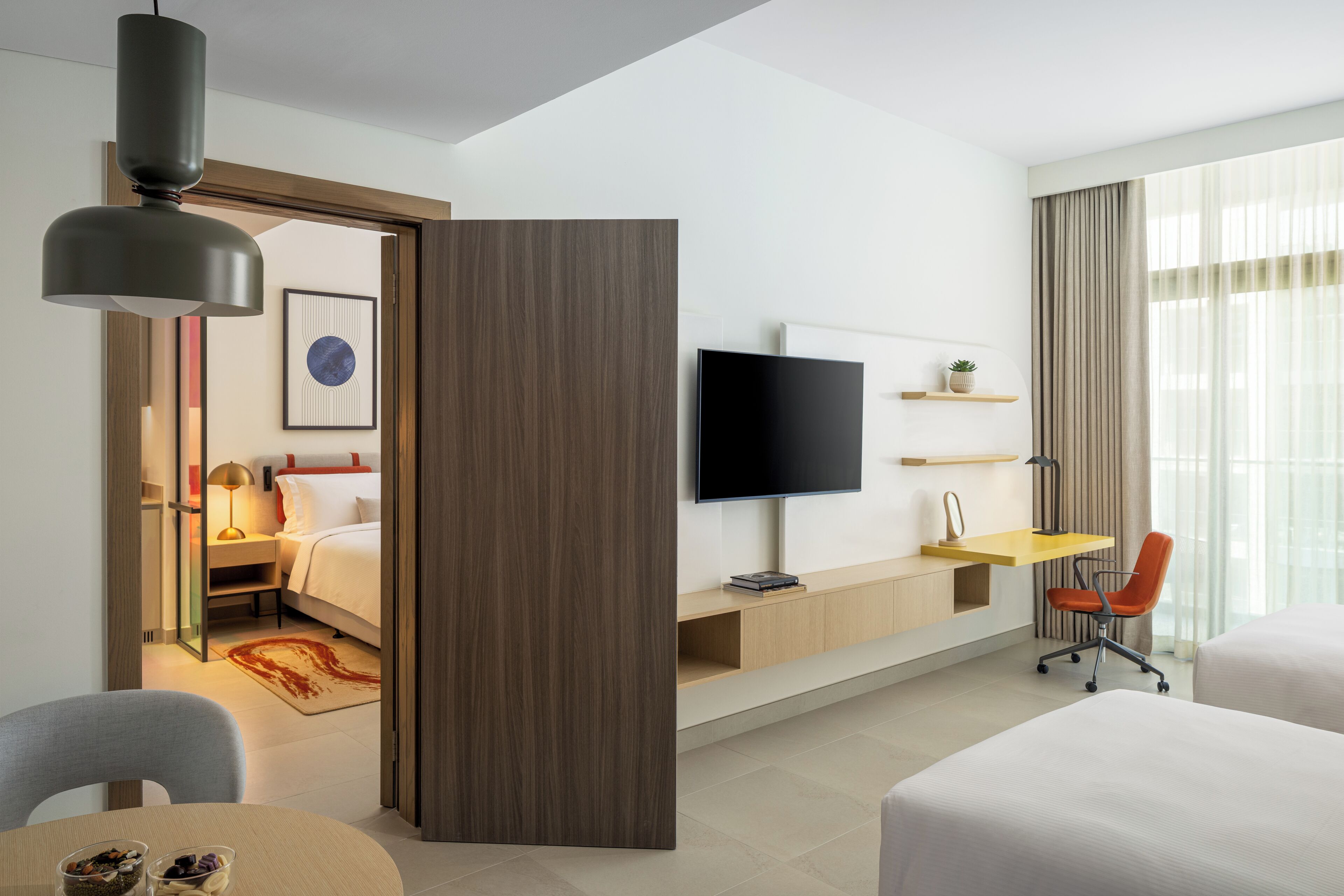 Ein Hotelzimmer mit Bett, Schreibtisch, Fernseher, Sessel und Esstisch.