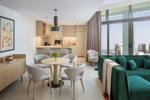 A modern apartment with a dining area, kitchen, and a green sofa with a view of the city.