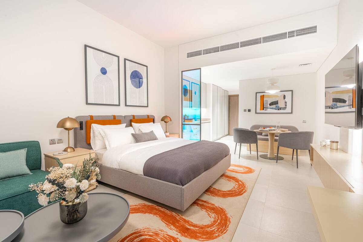 A modern hotel room with a bed, a desk, a sofa, and a dining area.