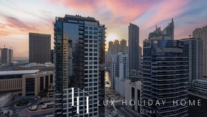 Een hoog gebouw met een modern architectonisch ontwerp, omringd door andere wolkenkrabbers, en een zonsonderganglucht.